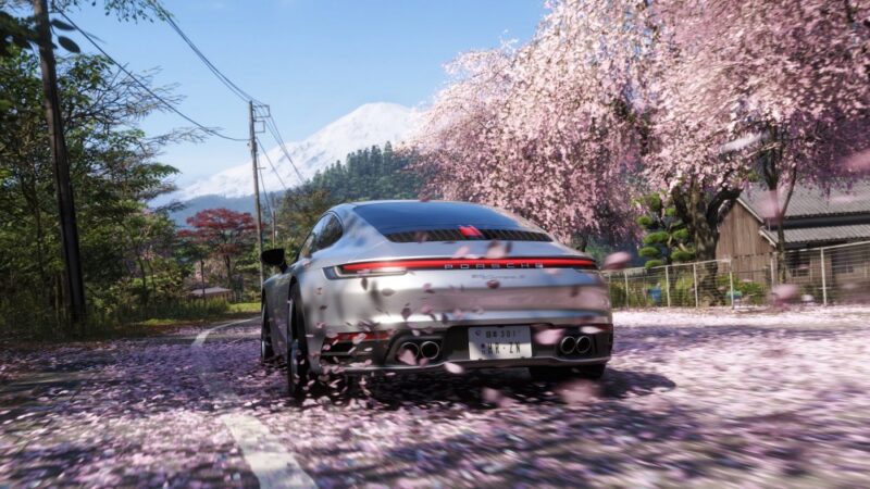 Co wiemy o Forza Horizon 6. Kadr przedstawia srebrne porsche pędzące asfaltową drogą w wiejskim krajobrazie Japonii. Pęd powietrza podnosi z drogi różowe płatki kwiatów wiśni.