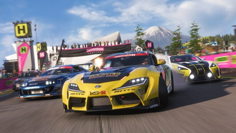 Co wiemy o Forza Horizon 6. Scena przedstawia kadr z szosowego wyścigu samochodowego w ramach Horizon Festival. Na czele znajduje się żółty samochód, za nim dwa kolejne auta usiłujące wyprzedzać, w tle ośnieżony szczyt góry.