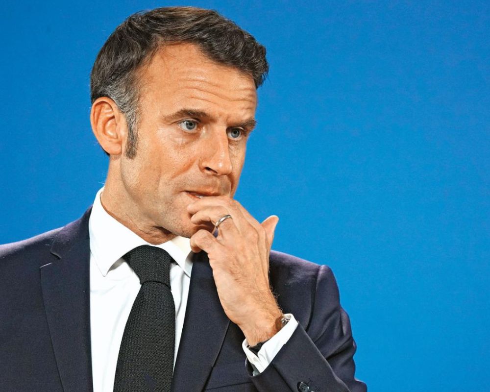 prezydent Francji, osoba dojrzała z brązowymi włosami, ubrana w granatowy garnitur, białą koszulę i czarnym krawatem na niebieskim tle