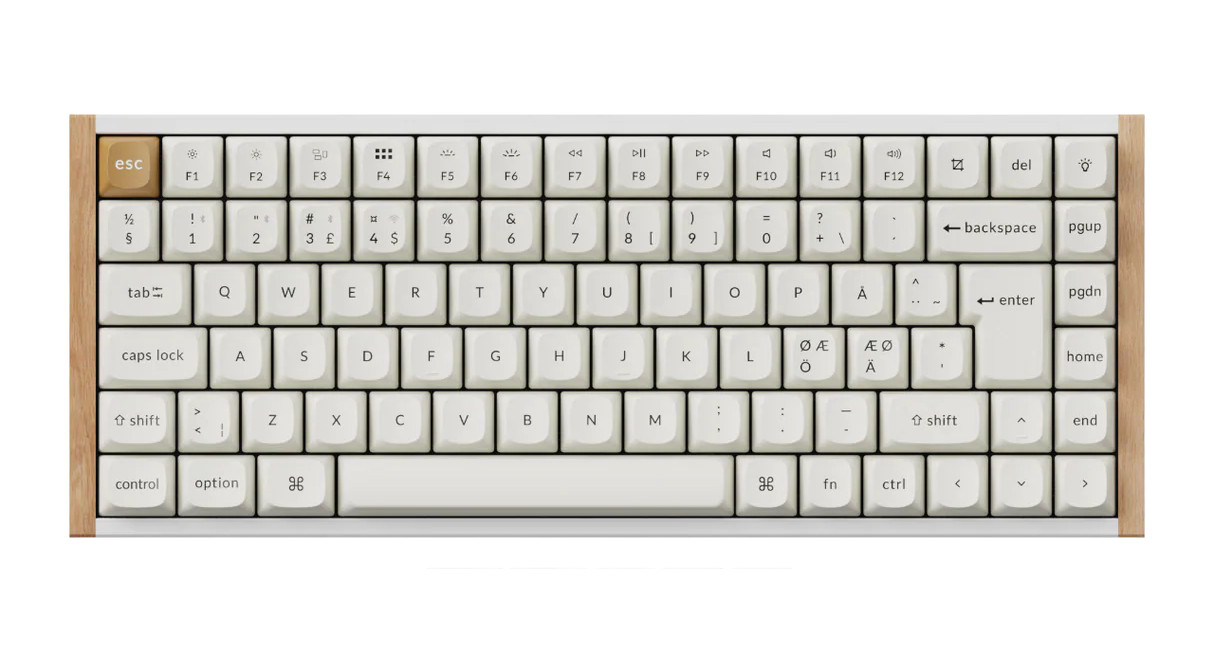 Zdjęcie prezentuje elegancką i minimalistyczną klawiaturę mechaniczną o kompaktowym układzie 75%, która wyróżnia się unikalnym połączeniem nowoczesnego wzornictwa z naturalnymi materiałami. Urządzenie posiada białą obudowę z charakterystycznymi drewnianymi panelami bocznymi o jasnym odcieniu, co nadaje mu luksusowy, ekologiczny wygląd. Klawisze mają kolor kremowy lub złamanej bieli, a ich zaokrąglone krawędzie i centralnie umieszczone napisy nawiązują do estetyki retro. Większość nakładek jest jednolita, z wyjątkiem klawisza Escape, który ma kolor musztardowy lub jasnobrązowy, harmonizujący z drewnianym wykończeniem. Układ klawiszy jest dostosowany do użytkowników systemów macOS i Windows (widoczne oznaczenia „option” i „command”), a brak bloku numerycznego sprawia, że klawiatura zajmuje niewiele miejsca na biurku, zachowując jednocześnie pełną funkcjonalność dzięki rzędowi klawiszy multimedialnych i dedykowanym przyciskom nawigacyjnym po prawej stronie.