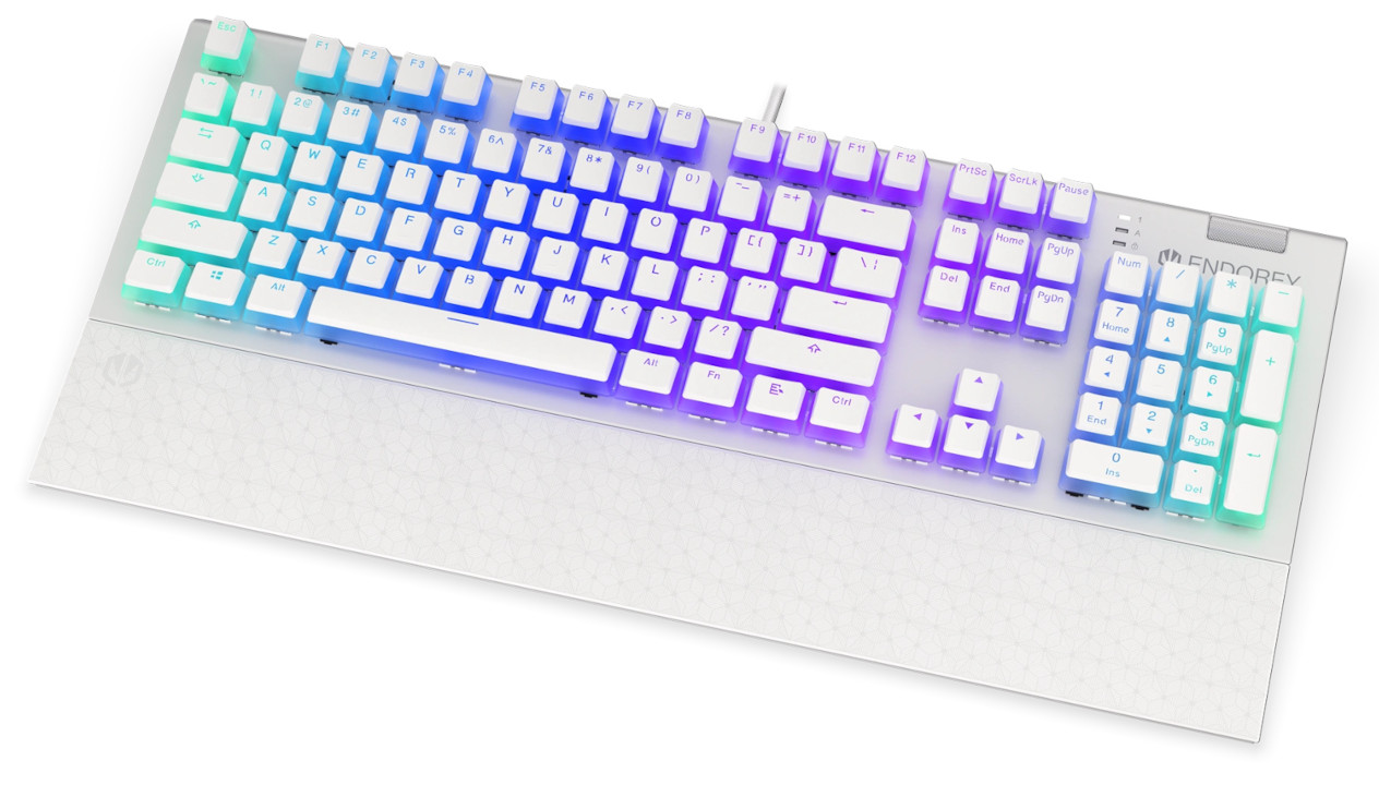Zdjęcie prezentuje białą, pełnowymiarową klawiaturę mechaniczną marki ENDORFY, wyposażoną w zintegrowaną podkładkę pod nadgarstki ozdobioną subtelnym, geometrycznym wzorem. Urządzenie charakteryzuje się efektownym podświetleniem RGB w chłodnych odcieniach błękitu, fioletu i mięty, które przenika przez półprzezroczyste ścianki klawiszy typu „pudding”, eksponując ich dolną część. Górny panel obudowy ma srebrzyste, metaliczne wykończenie, a w prawym górnym rogu znajduje się szeroka, metalowa rolka do regulacji głośności oraz logo producenta. Klawiatura posiada klasyczny układ z wydzieloną sekcją numeryczną i kursorami, a z jej środkowej części wychodzi biały przewód zasilający.
