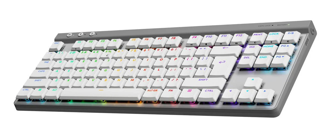 Zdjęcie przedstawia niskoprofilową, bezprzewodową klawiaturę mechaniczną marki Logitech (model G515 TKL) w eleganckiej, szaro-białej kolorystyce. Urządzenie posiada kompaktowy układ typu TKL (bez bloku numerycznego), z białymi nakładkami na klawisze osadzonymi na ciemnoszarej, matowej bazie. Podświetlenie RGB jest wyraźnie widoczne pod klawiszami, tworząc wielokolorową poświatę w odcieniach zieleni, żółci, czerwieni i błękitu. W lewym górnym rogu obudowy znajdują się trzy dedykowane, okrągłe przyciski funkcyjne (prawdopodobnie do sterowania łącznością i trybem gry), a po prawej stronie panelu górnego widoczne są diody kontrolne Caps Lock i stanu baterii oraz subtelne logo serii „G”. Konstrukcja charakteryzuje się bardzo smukłym profilem i nowoczesnym designem, typowym dla sprzętu gamingowego klasy premium.
