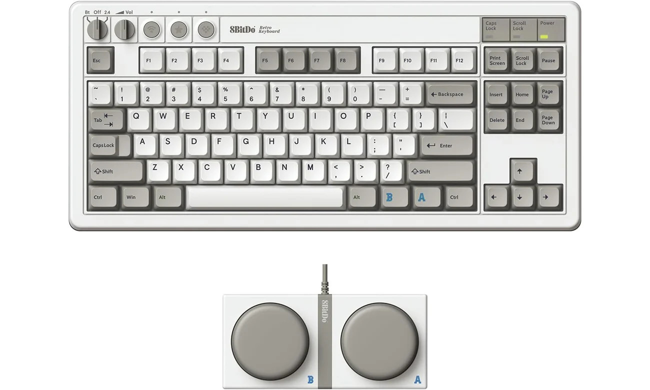 Zdjęcie prezentuje bezprzewodową klawiaturę mechaniczną marki 8BitDo w stylu retro, której design nawiązuje do klasycznych konsol do gier, takich jak Nintendo Entertainment System (NES). Urządzenie ma białą obudowę z szarymi i ciemnoszarymi klawiszami, a w lewym górnym rogu posiada dwa charakterystyczne pokrętła (do wyboru trybu łączności Bluetooth/2.4G oraz regulacji głośności) oraz trzy czerwone przyciski funkcyjne. Klawiatura ma układ TKL (TenKeyLess) bez bloku numerycznego, a na klawiszach widoczne są oznaczenia w stylu vintage, w tym niebieskie litery „A” i „B” na dolnych przyciskach obok spacji. W zestawie znajduje się również osobny, przewodowy moduł z dwoma dużymi, okrągłymi, szarymi przyciskami programowalnymi, oznaczonymi tymi samymi niebieskimi literami, co dopełnia nostalgiczny charakter całego zestawu.