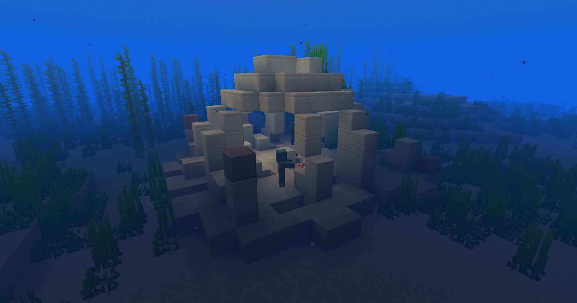 Zrzut ekranu z gry Minecraft przedstawiający podwodną ruinę. Na obrazku widzimy fragmenty budynku utworzonego z jasnych bloków piaskowca. Kształt budynku przypomina kopułę, ale ściany i podłoga struktury są wybrakowane. We wnętrzu stoi utopiec, zielony potwór przypominający zombie. Dookoła widać dno oceanu składające się z piasku, z gęsto rosnącymi wodorostami i glonami.