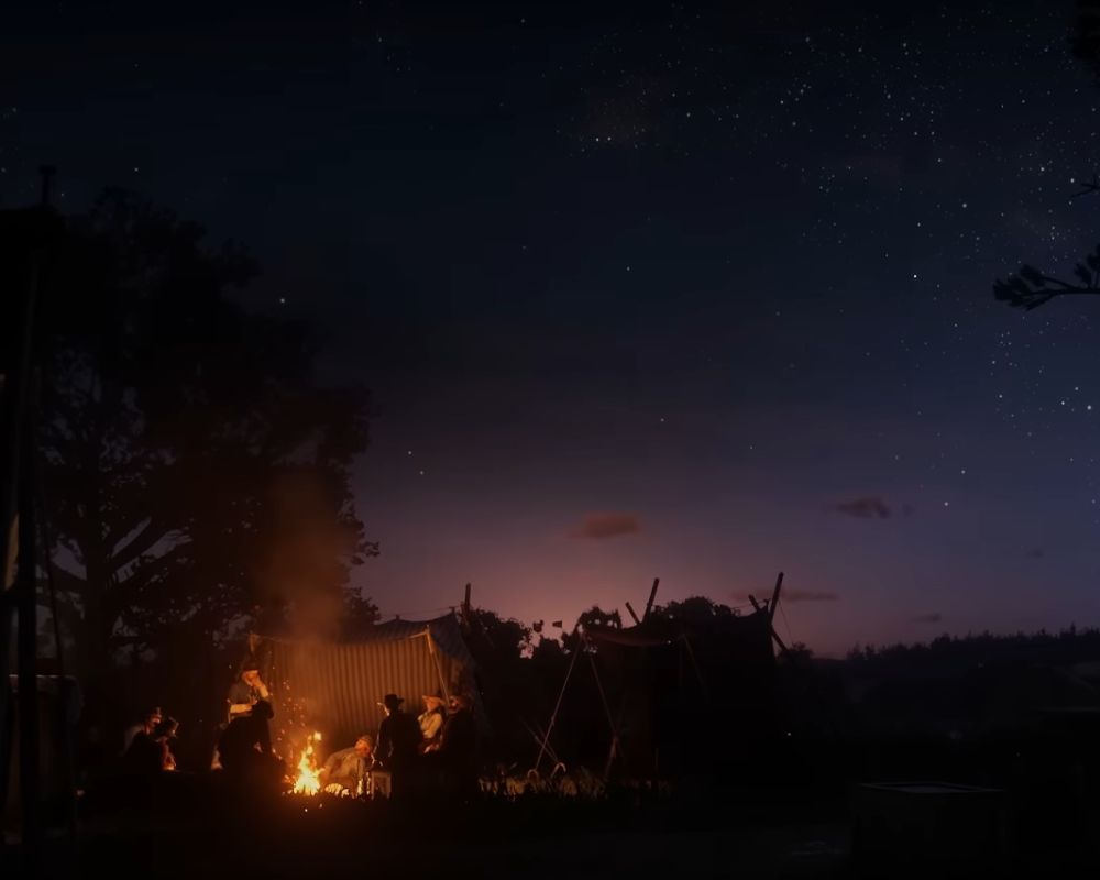 Fragment animacji z gry Red Dead Redemption 2, ukazująca, jak banda Dutcha siedzi w nocy przy ognisku. W tle widać jeszcze łunę zachodzącego słońca, a na niebie są już gwiazdy.