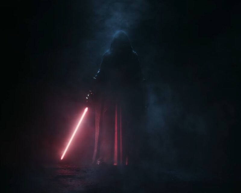 Zrzut ekranu ze zwiastuna kinowego remake'u gry Star Wars: Knights of the Old Republic. Prezentuje on zakapturzoną postać, Darth Revan, z czerwonym mieczem świetlnym, spowitą ciemnością i dymem lub mgłą.