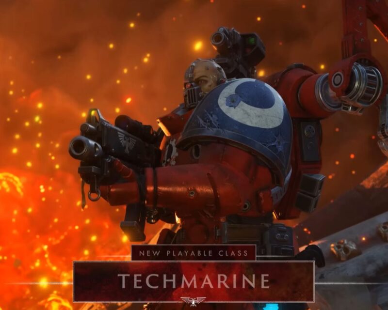 Kadr z gry Warhammer 40,000: Space Marine 2 zapowiadający nową aktualizację "Techmarine". Widoczna postać w charakterystycznym czerwonym pancerzu z elementami cybernetycznymi na twarzy, trzymająca broń dystansową. Nad ramieniem bohatera wystaje mechaniczne ramię konstrukcyjne. Postać stoi na tle ognia i iskier. W dolnej części widnieje napis: New Playable Class Techmarine.
