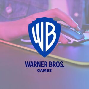 Logotyp Warner Bros. Games nałożony na zdjęcie dłoni gracza na myszce gamingowej. Logo to tarcza z literami 'WB' (białymi na niebieskim tle), pod którą znajduje się napis 'WARNER BROS. GAMES' w kolorze ciemnoniebieskim. Tło pokazuje dłoń w zbliżeniu na myszce z podświetleniem LED, na podkładce, w nastrojowym różowo-niebieskim świetle. Ilustracja sugeruje zwolnienia w Warner Bros. Montreal w 2026 roku