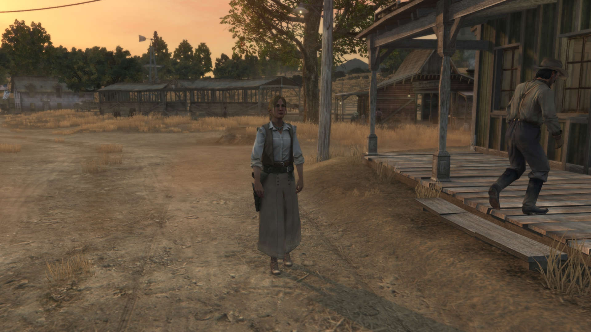 Kadr z gry Red Dead Redemption przedstawiający Bonnie MacFarlane stojącą na terenie rancza MacFarlane's Ranch o zachodzie słońca. Bonnie ma na sobie klasyczny strój z epoki: białą koszulę, brązową kamizelkę i długą, jasną spódnicę. W tle widoczne są drewniane zabudowania gospodarcze, zagrody dla zwierząt oraz nastrojowe, ciepłe światło kończącego się dnia. Po prawej stronie widać fragment ganku, na który wchodzi inna postać.