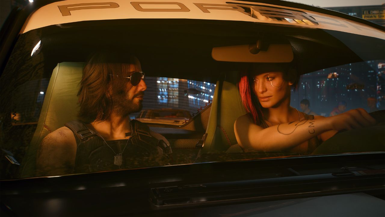Kobieca V i Johnny Silverhand siedzą w samochodzie w nocnym, neonowym mieście z gry Cyberpunk 2077. V znajduje się za kierownicą po prawej stronie kadru – ma krótkie czarne włosy z czerwonym pasmem oraz widoczne cybernetyczne implanty na skroni i tatuaż na ramieniu. Trzyma kierownicę i siedzi na miejscu kierowcy. Obok niej, na fotelu pasażera, siedzi Johnny Silverhand – mężczyzna z długimi włosami, brodą i ciemnymi okularami, ubrany w czarną kamizelkę.