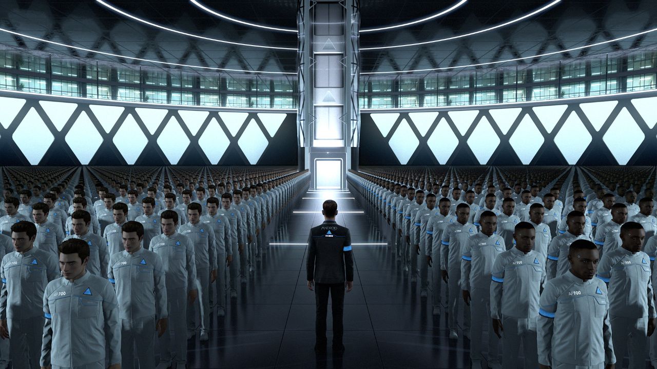 Scena z gry Detroit: Become Human przedstawiająca ogromną, futurystyczną halę produkcyjną pełną androidów stojących w długich, równych rzędach. Androidy ubrane są w białe uniformy z oznaczeniami modeli i niebieskimi trójkątami na piersi. Na środku przejścia stoi Connor – android w ciemnym garniturze z napisem „ANDROID” na plecach. Hala jest jasna i nowoczesna, z wysokim sufitem, metalowymi konstrukcjami i dużymi panelami świetlnymi na ścianach, które oświetlają symetrycznie ustawione rzędy androidów.