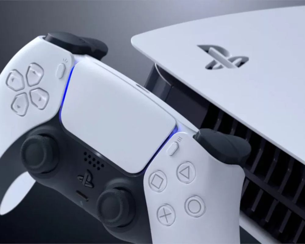 Biały pad DualSense obok konsoli PlayStation 5 z podświetleniem LED w niebieskim kolorze.