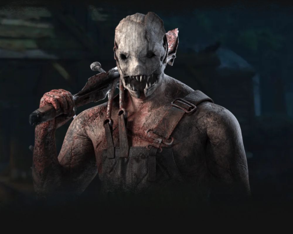 Zrzut ekranu z gry Dead by Daylight przedstawiający postać Trappera (Trapera). Widoczny jest od pasa w górę, ukazując jego potężną sylwetkę pokrytą bliznami i śladami krwi. Postać nosi charakterystyczną, przerażającą maskę zrobioną z kości lub metalu z rzędami ostrych zębów. Na ramieniu opiera swoją broń – zakrwawiony, prowizoryczny tasak. Postać ubrana jest w brudne, ciemne ogrodniczki, a całość utrzymana jest w mrocznej, ponurej kolorystyce.