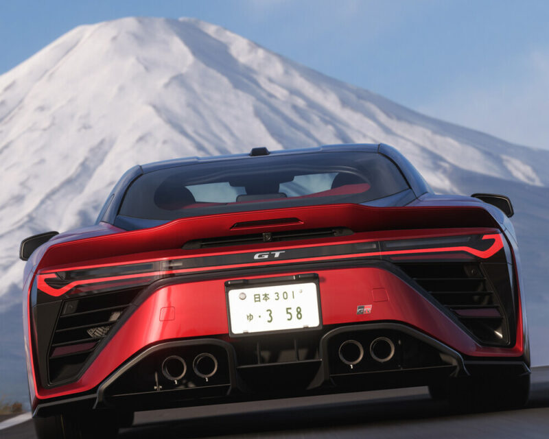 Obrazek przedstawia bardzo realistyczny kadr z gry, na którym główny plan zajmuje tył nowoczesnego, sportowego samochodu w lśniącym odcieniu czerwieni – jest to Toyota GR GT. Auto charakteryzuje się niezwykle agresywnym i aerodynamicznym designem, co podkreśla masywny, czarny dyfuzor z czterema rurami wydechowymi