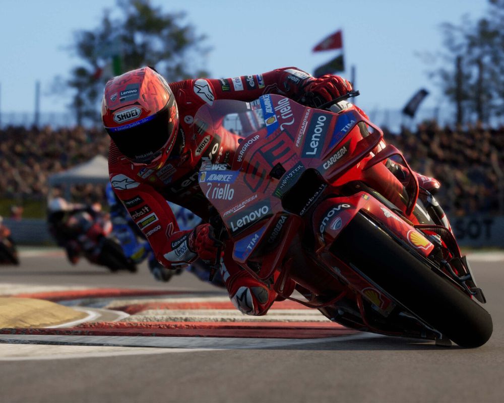 Motocyklista w czerwonym kombinezonie wyścigowym pokonuje ostry zakręt na torze wyścigowym, mocno pochylając motocykl sportowy. Na maszynie widoczne są logotypy sponsorów, a w tle znajdują się inni zawodnicy oraz trybuny z widzami. Scena przedstawia dynamiczny moment wyścigu motocyklowego w realistycznym stylu.