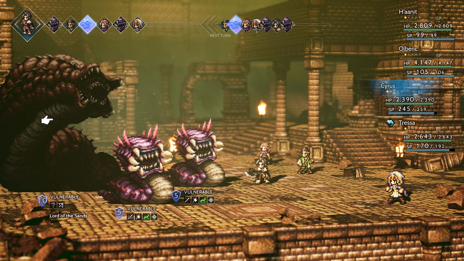 Zrzut ekranu z gry Octopath Traveler prezentuje turowy system walki. Po lewej stronie widoczny jest potężny przeciwnik o nazwie Lord of the Sands w towarzystwie mniejszych potworów, nad którymi wyświetlają się liczniki słabości i statusy Vulnerable. Po prawej stronie znajdują się czterej bohaterowie — H'aanit, Olberic, Cyrus i Tressa — wraz z ich statystykami HP i SP widocznymi w górnym rogu interfejsu. Sceneria starcia to skąpane w ciepłym, pustynnym świetle kamienne ruiny z antycznymi kolumnami i nastrojowym oświetleniem pochodni. Grafika oddaje dynamiczny klimat klasycznego JRPG, wykorzystując charakterystyczny efekt głębi ostrości, który nadaje całości kinowy charakter.