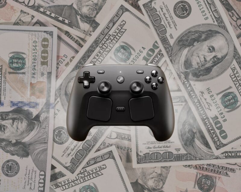 Czarny kontroler Valve Steam Controller na tle rozrzuconych banknotów 100 dolarów amerykańskich. Grafika sugeruje wysoką cenę Steam Controller