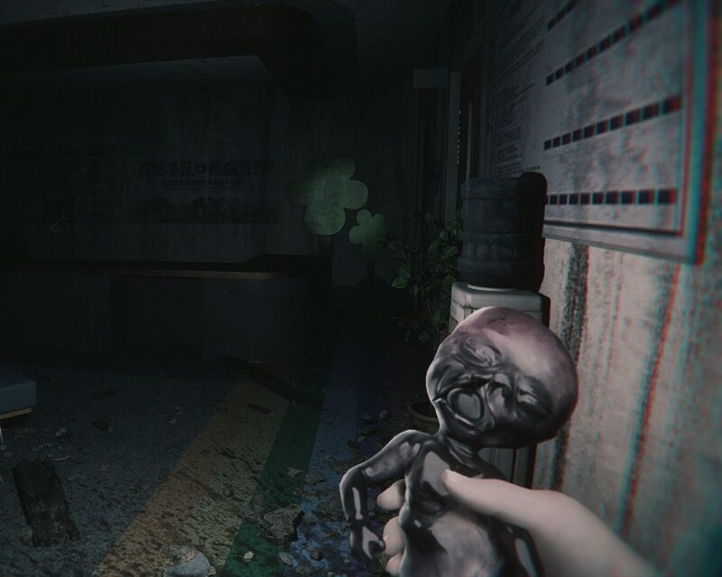 Mroczna scena z gry horrorowej przedstawiająca dłoń trzymającą małą, zniszczoną figurkę przypominającą dziecko lub lalkę. W tle widoczny jest opuszczony, zaniedbany korytarz z dystrybutorem wody, rośliną w doniczce oraz tablicą informacyjną na ścianie. Całość utrzymana jest w ciemnym, niepokojącym klimacie, sugerującym atmosferę grozy i tajemnicy.