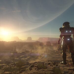 Zrzut ekranu z gry Mass Effect: Andromeda, widzimy na nim krajobraz jednej z planet. Jest pustynny, nad piaszczysto-skalną powierzchnią unosi się kurz, w tle widać wschodzące lub zachodzące słońce, a także zarys jakiejś innej planety lub gwiazdy. Na pierwszym planie, tyłem do widza, nieco z boku stoi postać w bojowym skafandrze kosmicznym. Na plecach znajdują się trzy świecące na niebiesko lampki