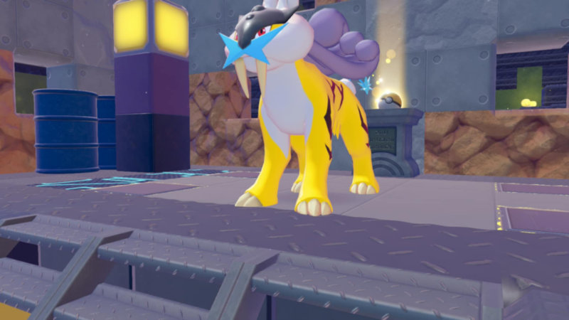 Stylizowana scena w kolorowej, lekko bajkowej estetyce przedstawia dużego, żółtego Pokemona przypominającego tygrysa stojącego na metalowej platformie. Otoczenie ma industrialny charakter, z widocznymi panelami, beczkami i oświetleniem w tle. Postać jest centralnym punktem kadru.