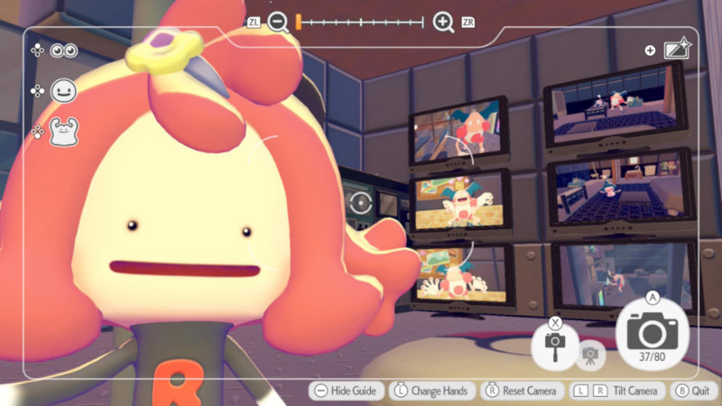 Postać gracza w grze Pokopia pozuje do zdjęcia typu selfie. Zaraz za nią widoczne są ekrany TV, na których znajdują się różne kadry z udziałem Pokemona Mr Mime. Całość stylizowana jest na pokój obsługi monitoringu.