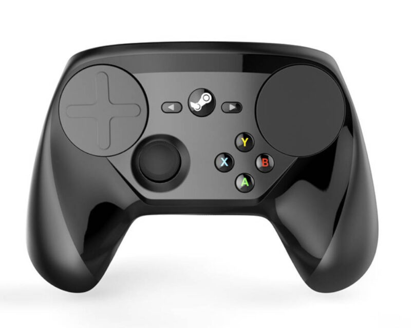 Zdjęcie przedstawia czarny, błyszczący kontroler do gier Steam Controller, umieszczony na jednolitym białym tle. Urządzenie charakteryzuje się unikalnym układem elementów sterujących, w którym dominują dwa duże, okrągłe panele dotykowe (trackpady) umieszczone po bokach górnej części obudowy, z których lewy posiada wytłoczony kształt krzyżaka (D-pad). Pomiędzy panelami, w centralnym punkcie, znajduje się okrągły przycisk z logo Steam, a po jego bokach dwa mniejsze przyciski funkcyjne ze strzałkami. Poniżej lewego panelu dotykowego umieszczono pojedynczą gałkę analogową, natomiast po prawej stronie znajduje się zestaw czterech kolorowych przycisków akcji oznaczonych literami A (zielony), B (czerwony), X (niebieski) i Y (żółty).