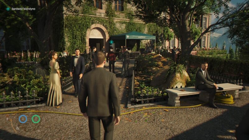 Screen z gry 007 First Light przedstawiający Jamesa Bonda zbliżającego się do budynku. przypominającego hotel. Wkoło wiele schludnie ubranych postaci i sporo zieleni takich jak drzewa, krzewy czy porośnięte ściany budynku.