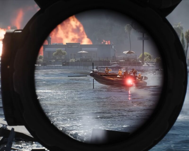 Kadr z perspektywy pierwszej osoby z gry Battlefield, ukazujący widok przez okrągły, czarny celownik snajperski lub optyczny. Centralnym punktem są czarne linie siatki celowniczej (krzyż), wycelowane w płynącą po wzburzonej wodzie motorową łódź hybrydową (ponton RIB). Na pokładzie łodzi znajduje się kilku uzbrojonych żołnierzy w pełnym rynsztunku bojowym, a z boku burty widać uchwycony, przelatujący pocisk w kolorze czerwonym. W tle, na drugim brzegu, widoczne jest nadmorskie miasteczko z palmami oraz parterowy budynek, za którym unoszą się potężne, pomarańczowe płomienie i gęsty dym z ogromnego pożaru.