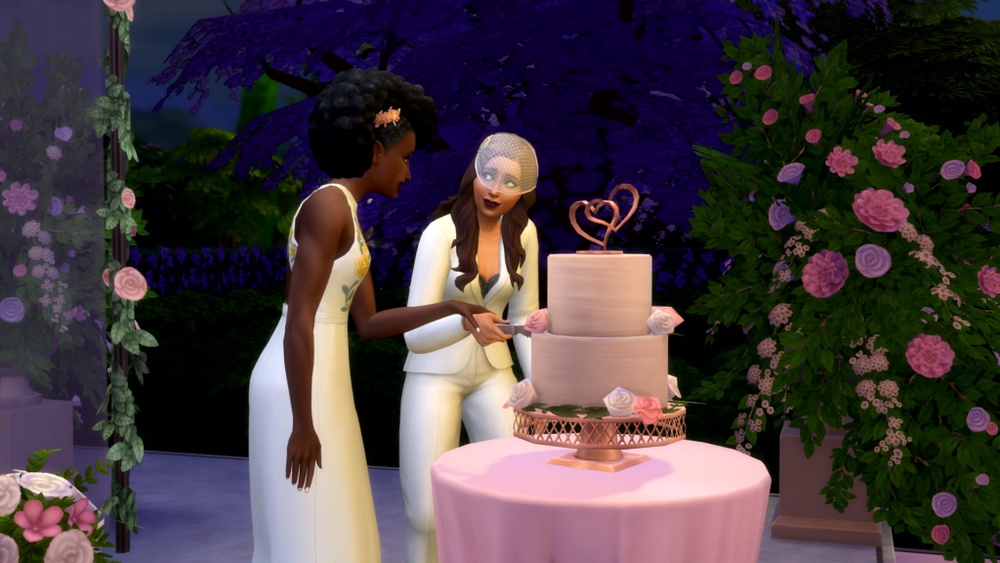 Zrzut ekranu z gry The Sims 4 przedstawiający scenę ślubu dwóch kobiet. Jedna z nich ubrana jest w jasną suknię ślubną z kwiatowym zdobieniem. Druga ubrana jest w biały garnitur. Razem kroją dwupiętrowy tort weselny w kolorze różowego beżu, zwieńczony złotą dekoracją w kształcie dwóch serc. Tort stoi na różowym okrągłym stole. W tle widoczne są fioletowe drzewa oraz dekoracje kwiatowe w odcieniach różu i bieli.