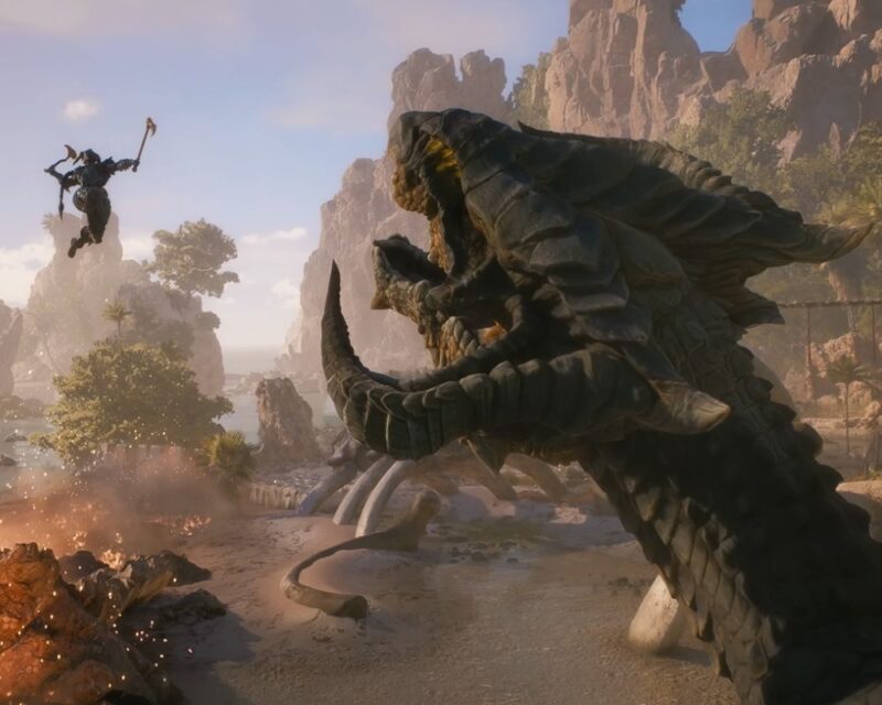 Zrzut ekranu z gry "Dragon Age: The Veilguard" przedstawia dynamiczną scenę walki na piaszczystej plaży otoczonej skalistymi klifami i zieloną roślinnością. Na pierwszym planie po prawej stronie widać potężną głowę smoka o ciemnych łuskach i otwartej paszczy z żółtymi oczami. W tle po lewej stronie widać postać Taash w zbroi, które wznosi się w powietrze, wykonując atak toporem w kierunku smoka. Na plaży widać szczątki szkieletów oraz niewielki ogień po lewej stronie. W tle widać morze oraz jasne niebo.