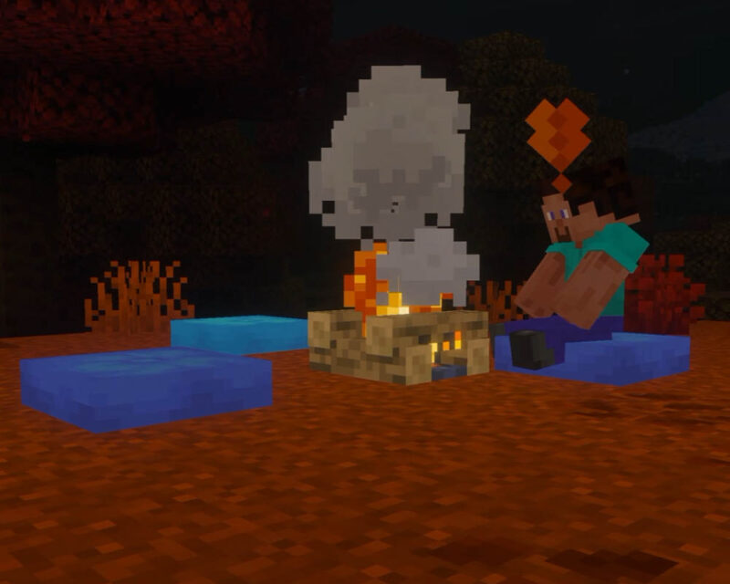 Grafika przedstawia scenę z gry Minecraft, rozgrywającą się nocą na otwartej przestrzeni o pomarańczowo-brązowym podłożu. W centrum kadru znajduje się płonące ognisko, z którego unoszą się gęste, szare kłęby dymu o charakterystycznym dla gry, pikselowym kształcie. Po prawej stronie ogniska siedzi postać Steve'a, ubrana w jasnoniebieską koszulkę i ciemnoniebieskie spodnie. Steve siedzi bezpośrednio na niebieskiej poduszce, a nad jego głową unosi się pomarańczowa ikonka przypominająca wykrzyknik lub znacznik interakcji. Wokół ogniska rozłożone są jeszcze dwie inne poduszki w odcieniach niebieskiego – jedna na pierwszym planie po lewej stronie, a druga nieco głębiej. W tle, za ogniskiem i postacią, widoczne są ciemne sylwetki drzew oraz rzadkie, pomarańczowo-czerwone zarośla, co nadaje całości klimat nocnego biwaku.